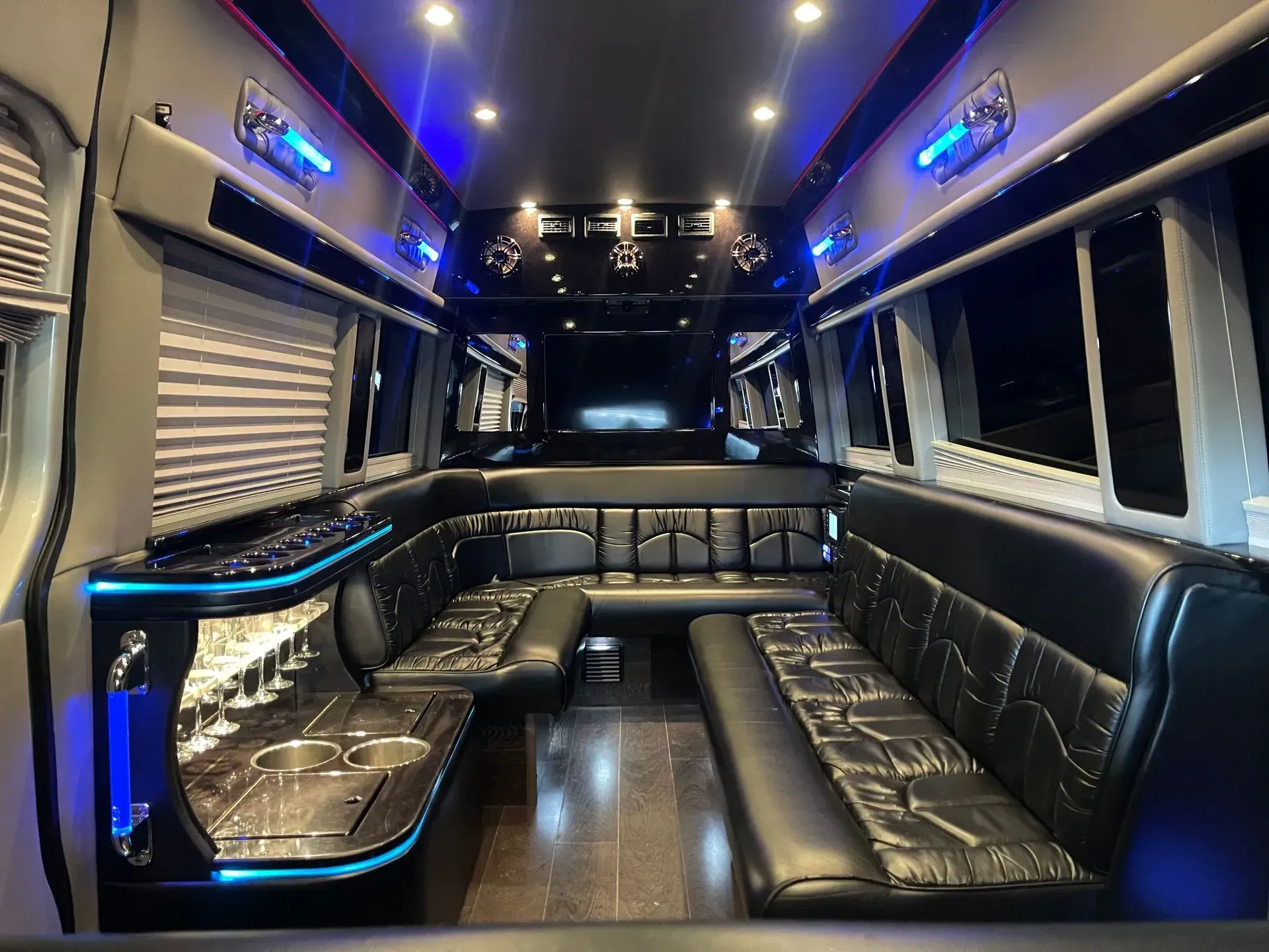 Interior of a party bus with black leather seating, blue lights, and a bar area.
