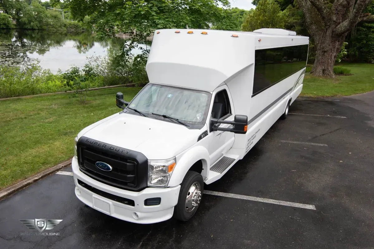 White passenger bus parked on asphalt, near a grassy area and body of water.