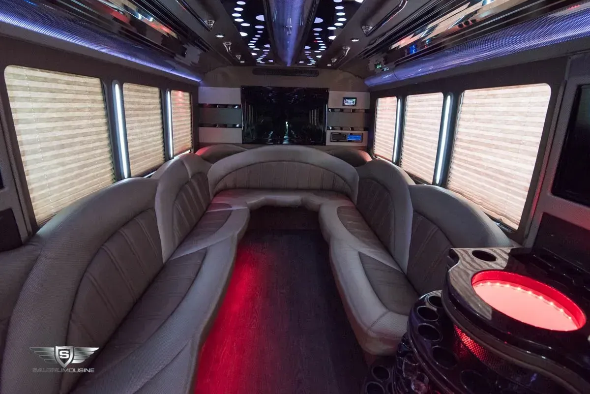 Interior of a luxury party bus with leather seating, red and blue lighting, and window shades.