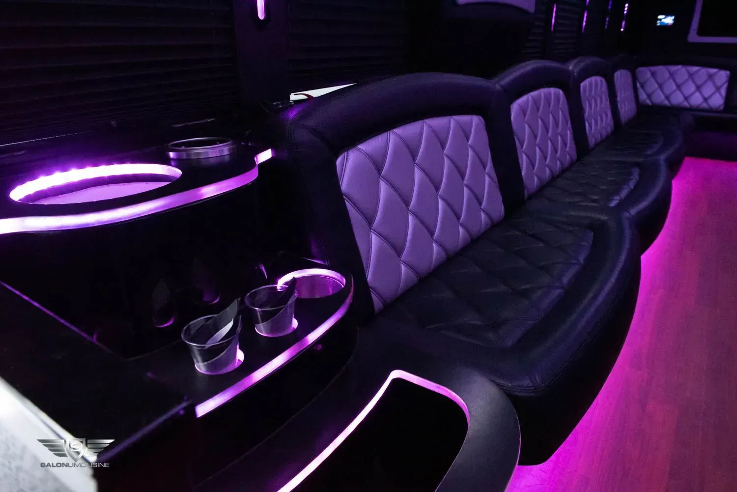 Interior of a limousine with purple lighting; black leather seats with quilted accents, cup holders.