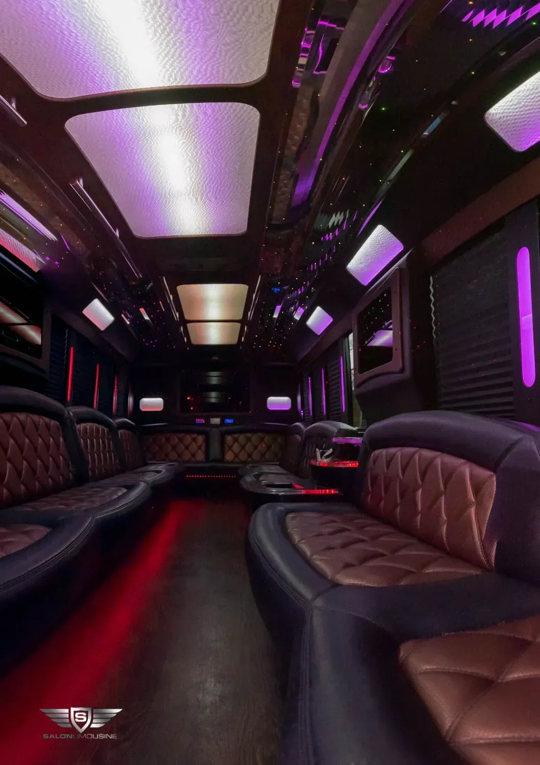 Inside of a luxury limousine with purple and red lighting, leather seating, and bar area.