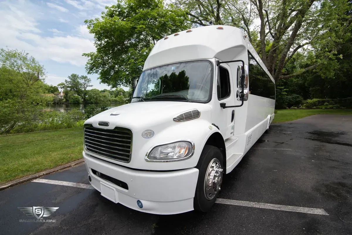 White passenger bus parked near trees and a body of water.