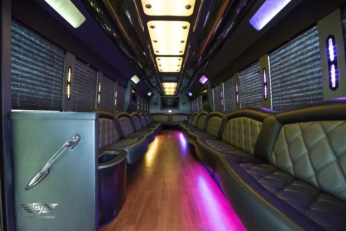 Inside of a luxury party bus with leather seating, wood floor, and neon lights.