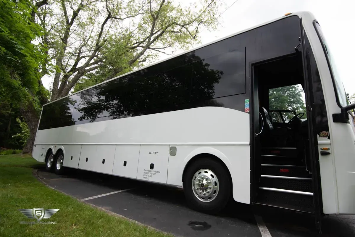 White charter bus with open door parked on asphalt next to grass and trees.