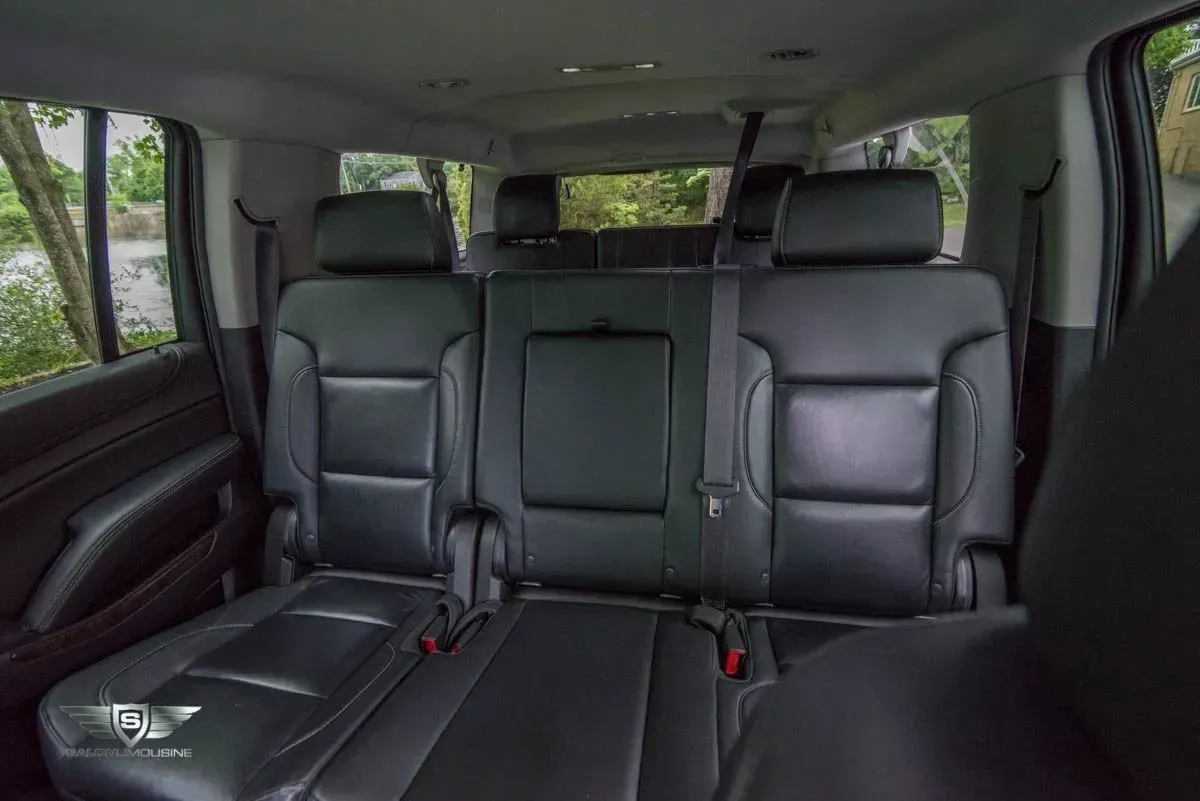 Rear seats of a black SUV, leather upholstery, three seats in the middle row, light outside the windows.