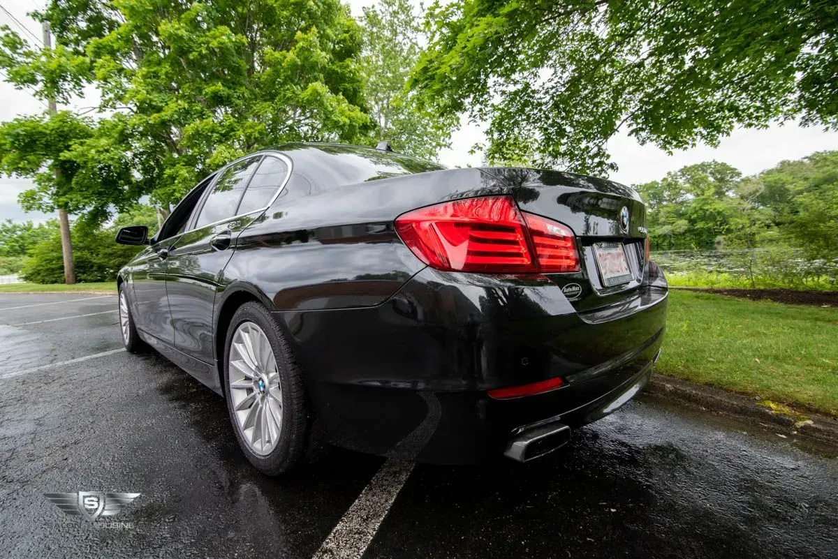 Black BMW sedan parked on wet asphalt, trees in the background.