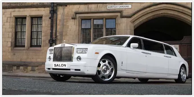 White Rolls Royce limousine parked in front of a stone building.