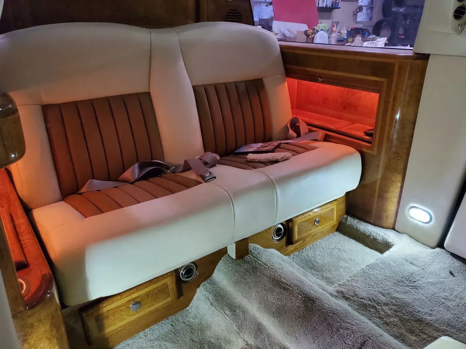 Luxurious car interior: White and tan leather seats with wood accents, seatbelts, and red ambient lighting.