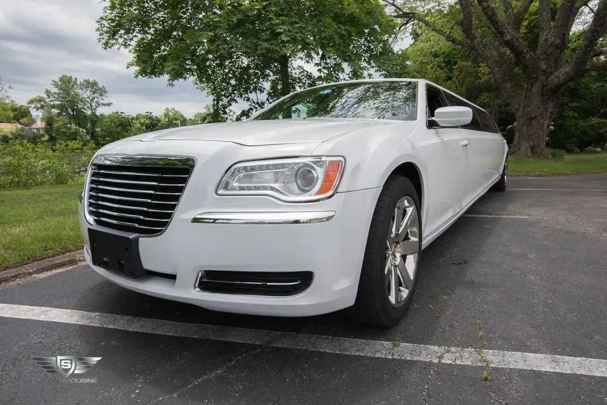 White Chrysler 300 limousine parked on asphalt. Tree and grass in background.