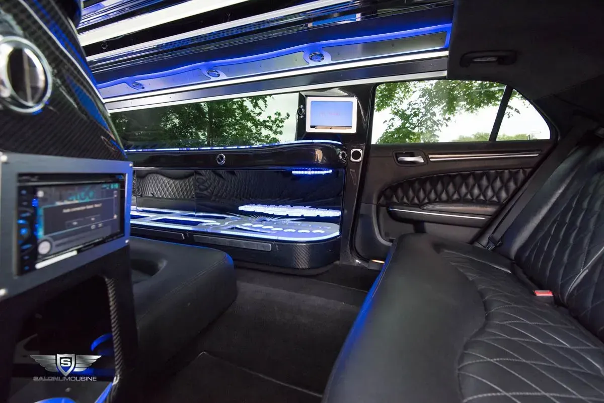 Interior of a limousine with black leather seats, blue lights, a monitor, and a sound system.
