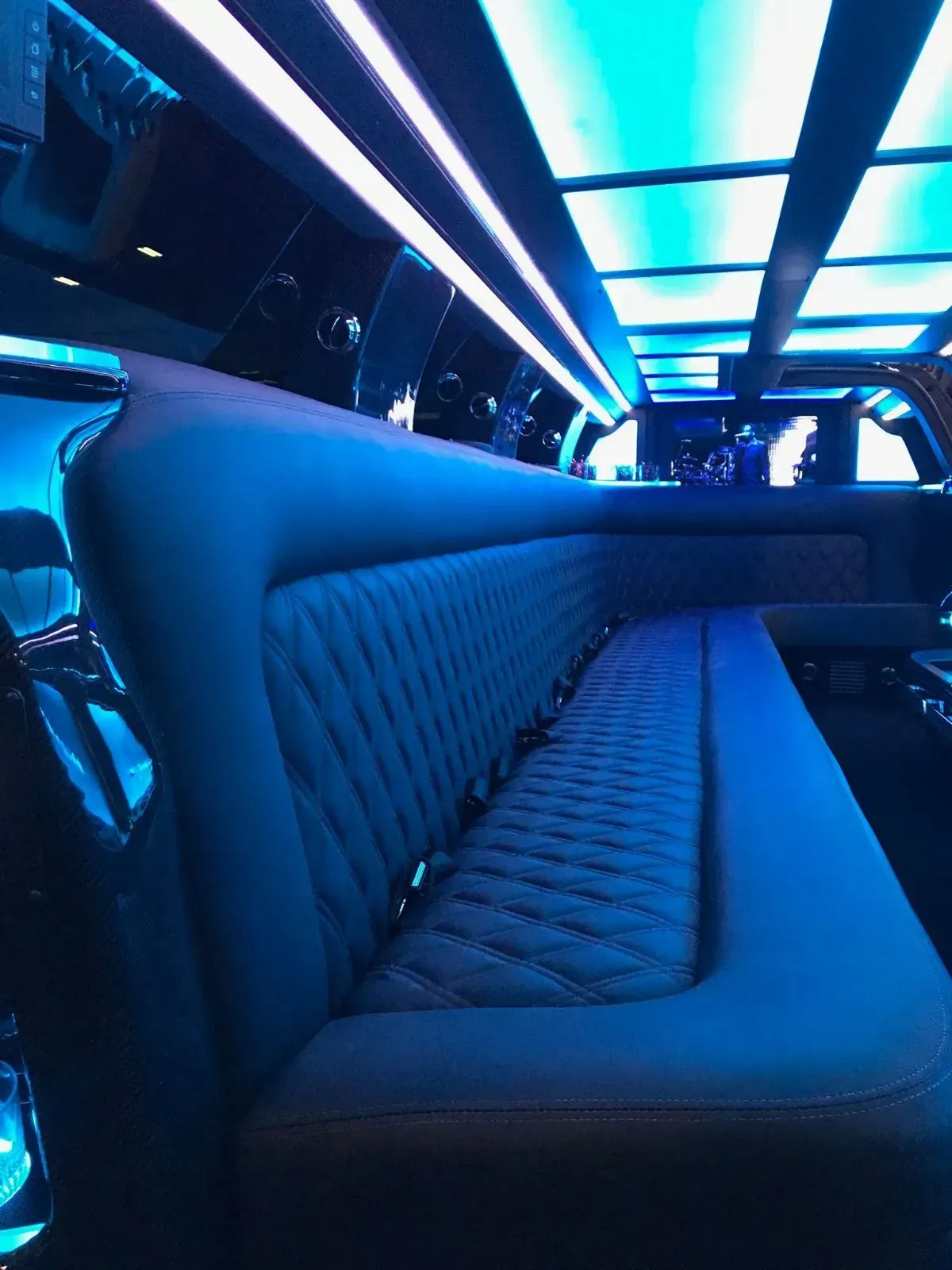 Interior of a limousine with blue illuminated ceiling and quilted leather bench seating.