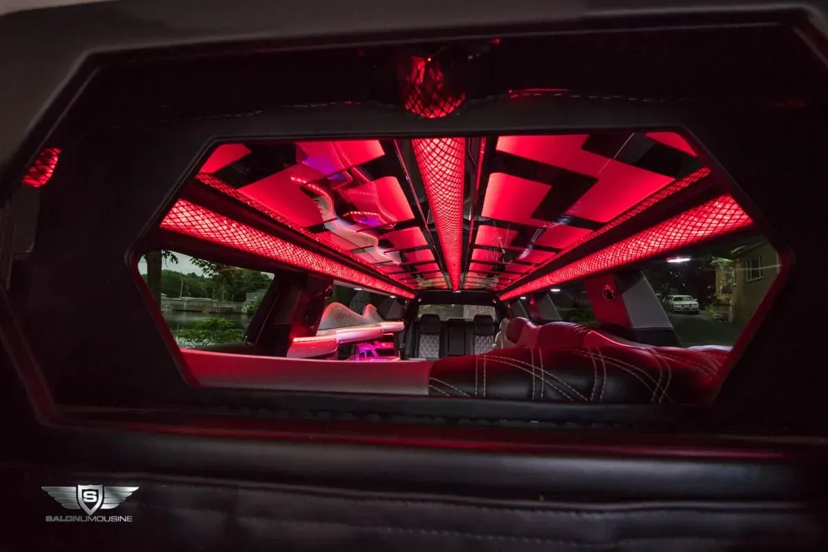 Interior of a limousine with red lights. Black leather seating, illuminated ceiling, and a partition window.