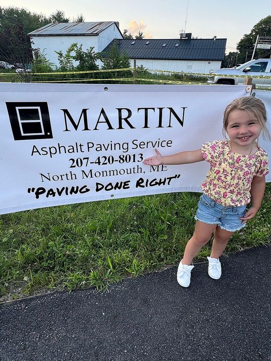 A little girl is standing in front of a Martin asphalt paving service sign.