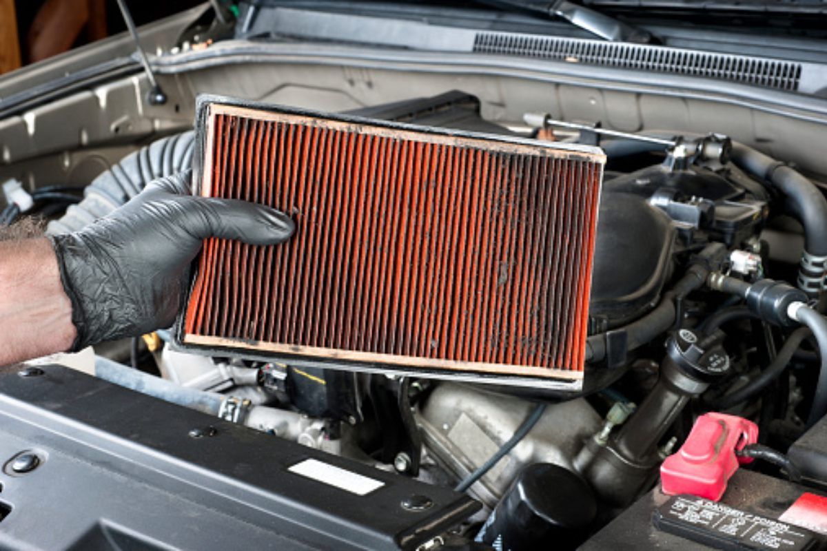 a person is holding an air filter in front of a car engine