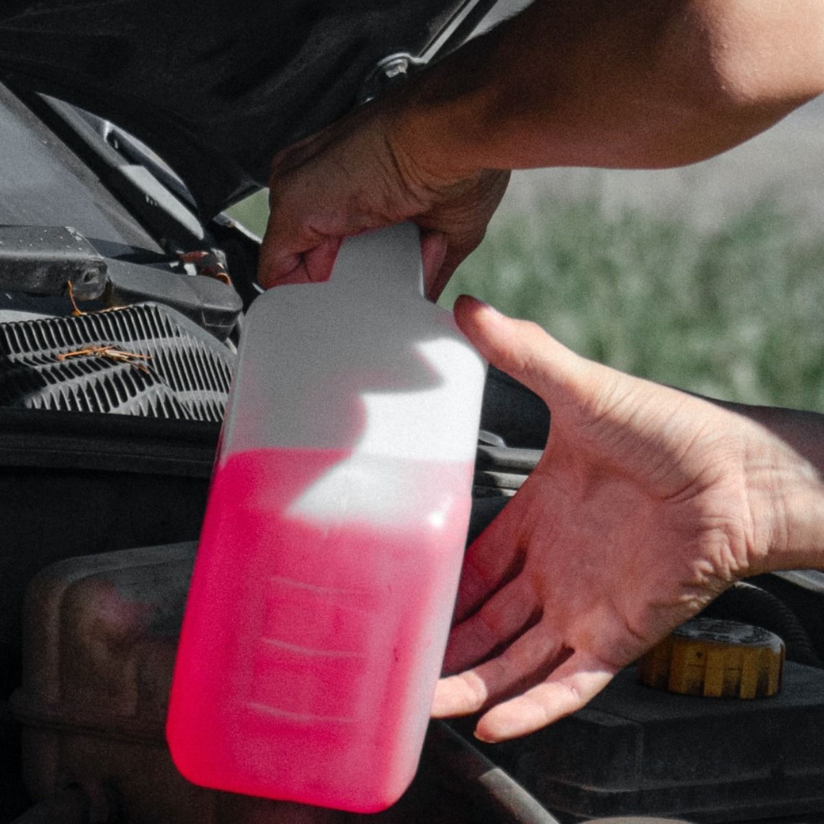 a person is holding a bottle of pink liquid under the hood of a car