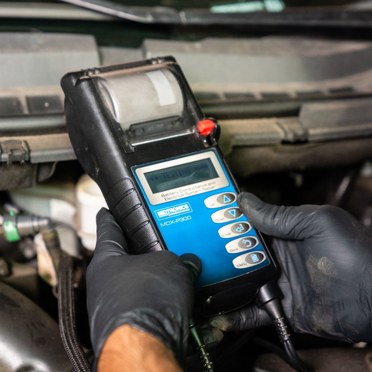 a person wearing black gloves is holding a device in front of a car engine