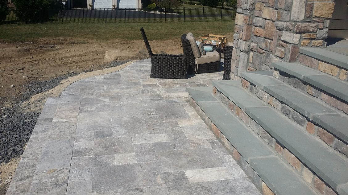 A patio with a chair and steps next to a stone wall.