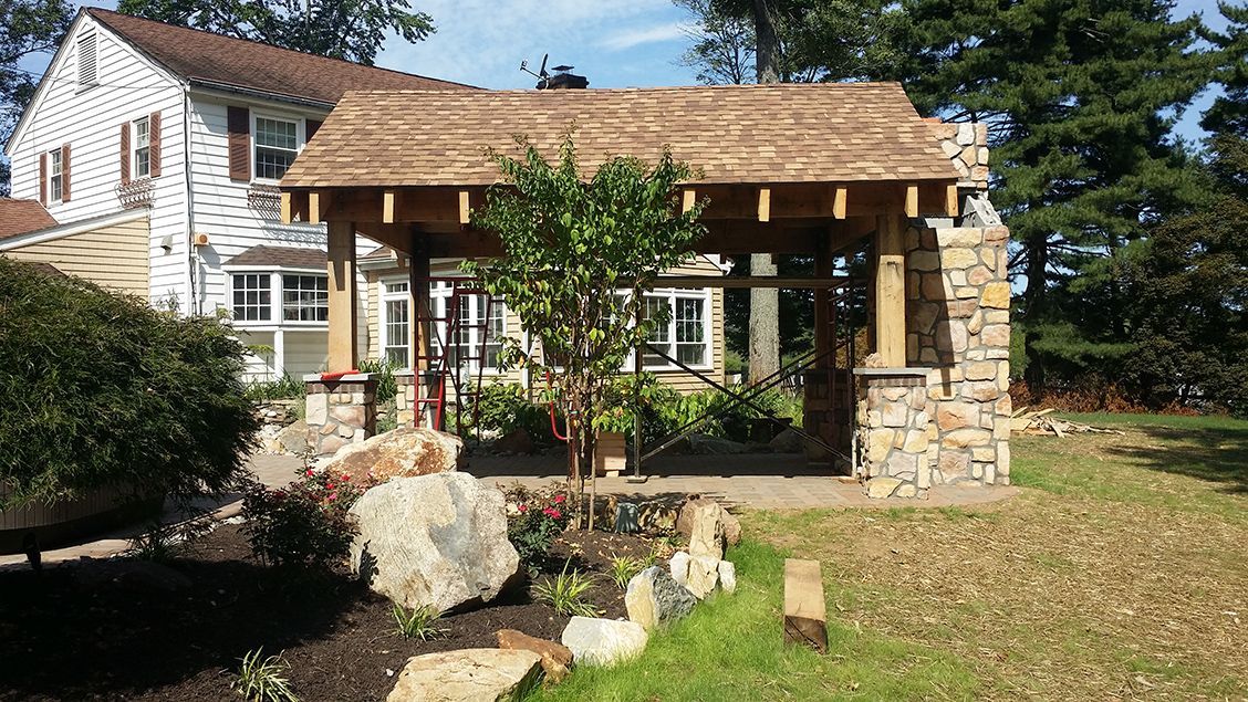 A house with a wooden roof is surrounded by trees and rocks.