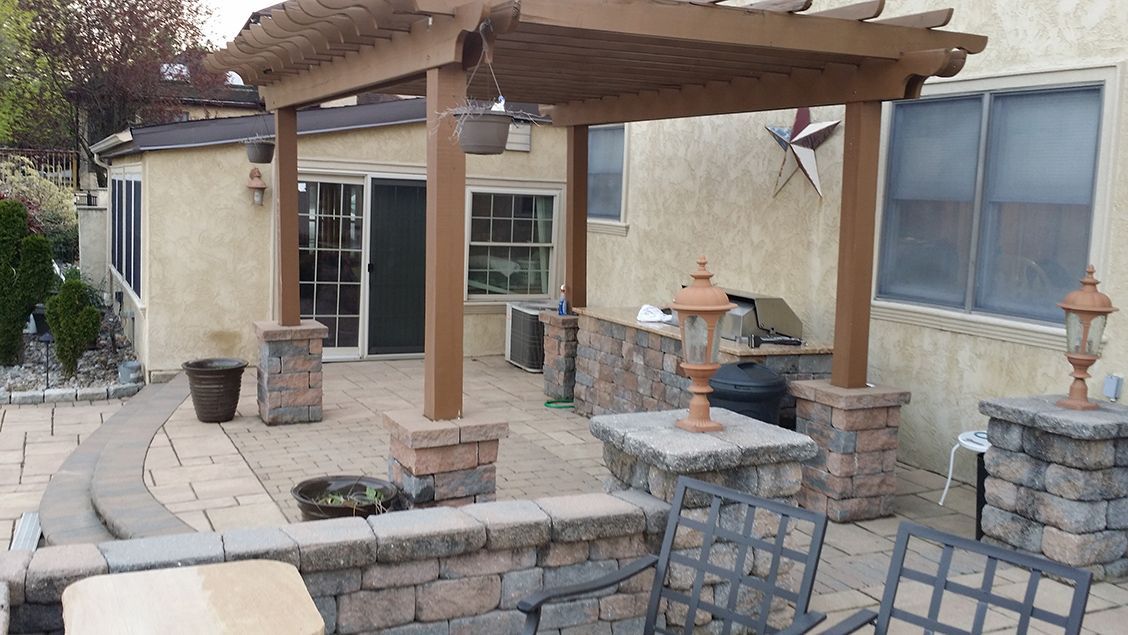 A patio with a pergola , table , chairs and a grill.