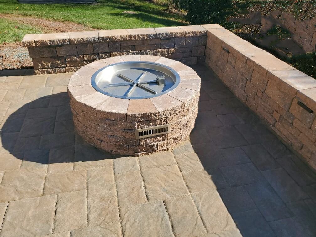 A fire pit is sitting on a brick patio next to a brick wall.