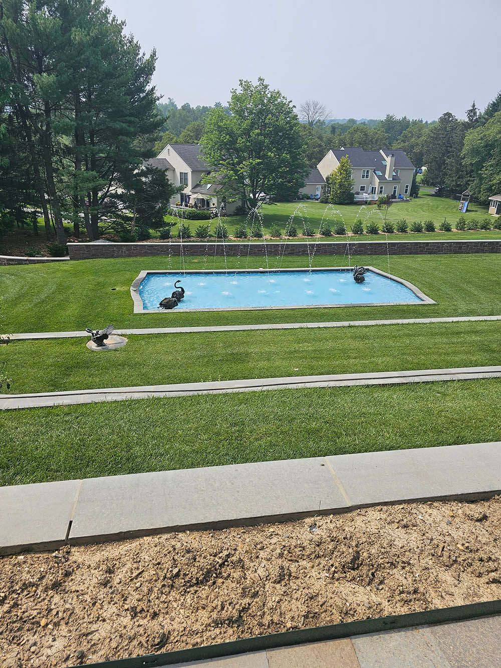 There is a large swimming pool in the middle of a lush green field.