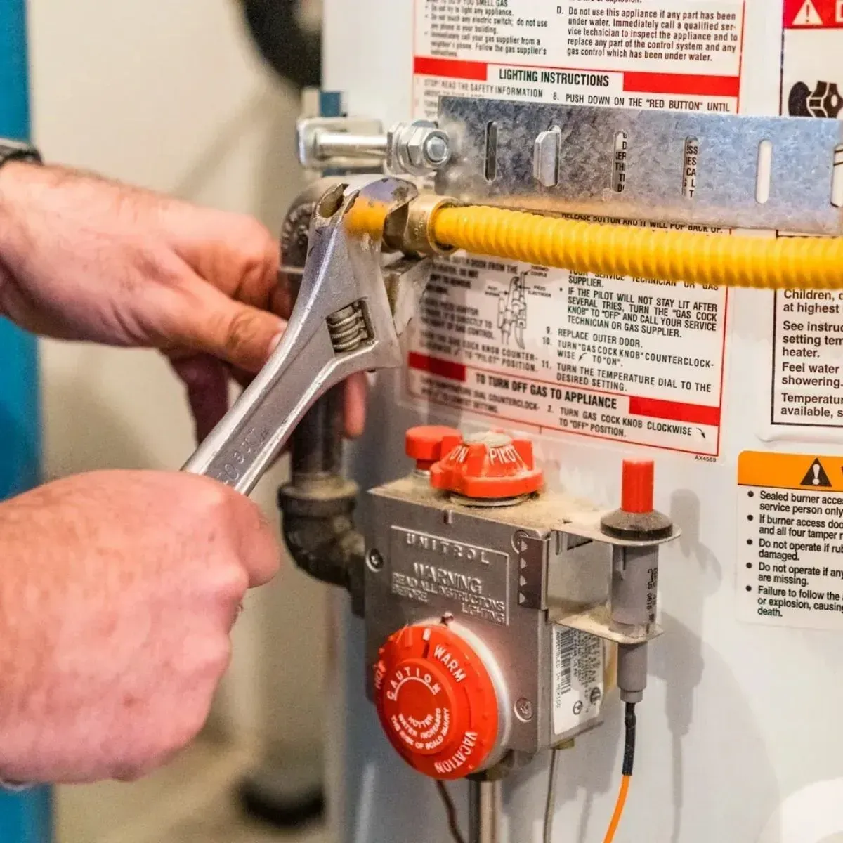 Hands using a wrench to adjust a gas water heater valve and yellow flexible gas line