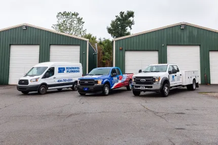 Three service vehicles parked in front of two green garage buildings.