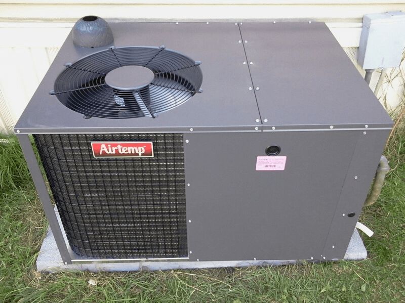 An air conditioner is sitting in the grass outside of a house.