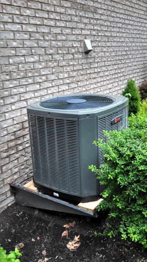 A large air conditioner is sitting on the side of a brick building.