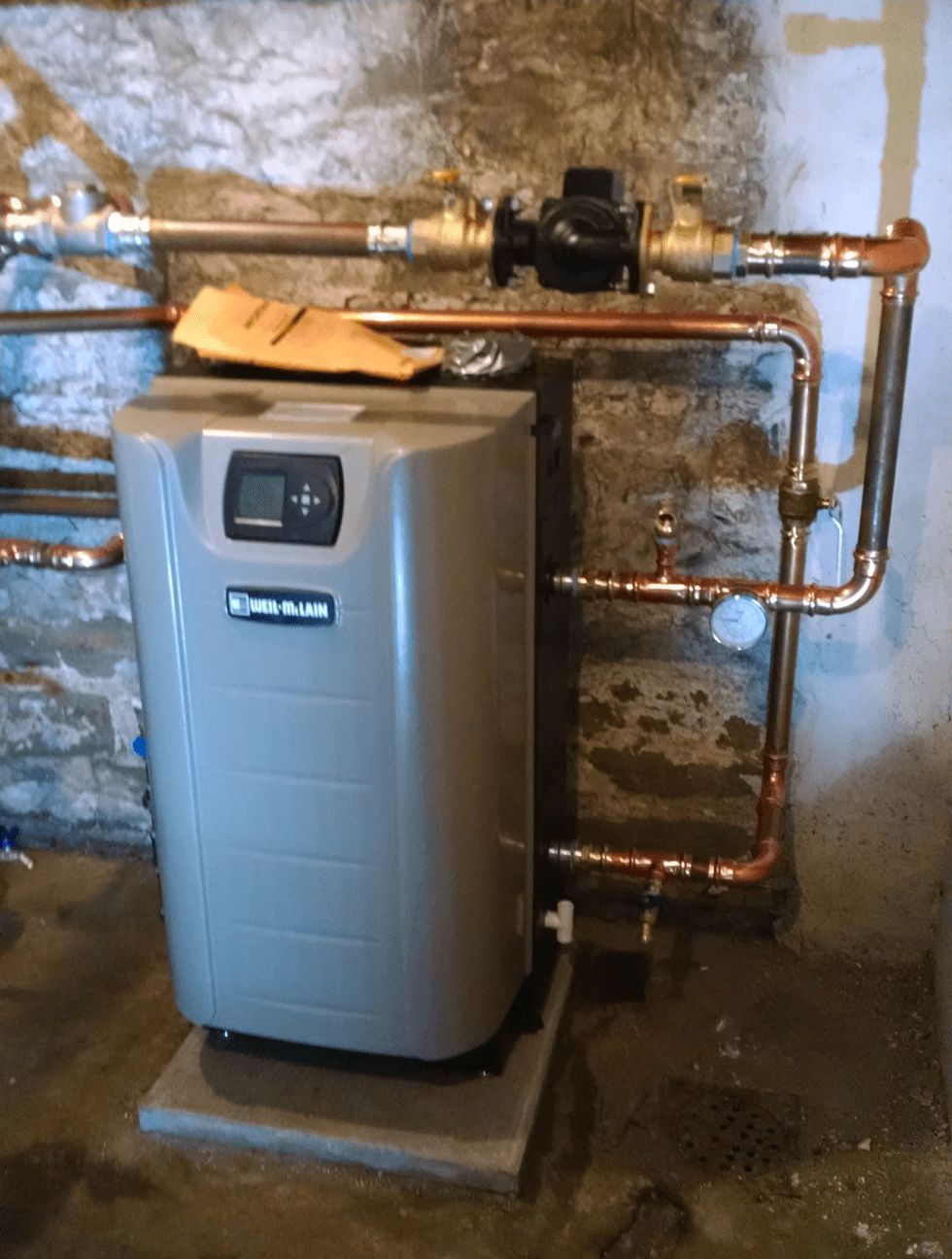 A water heater is sitting in a basement next to copper pipes.