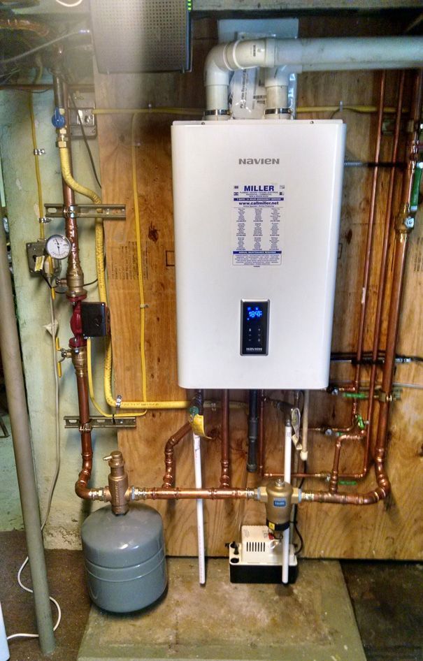 A white water heater is installed in a basement next to copper pipes.