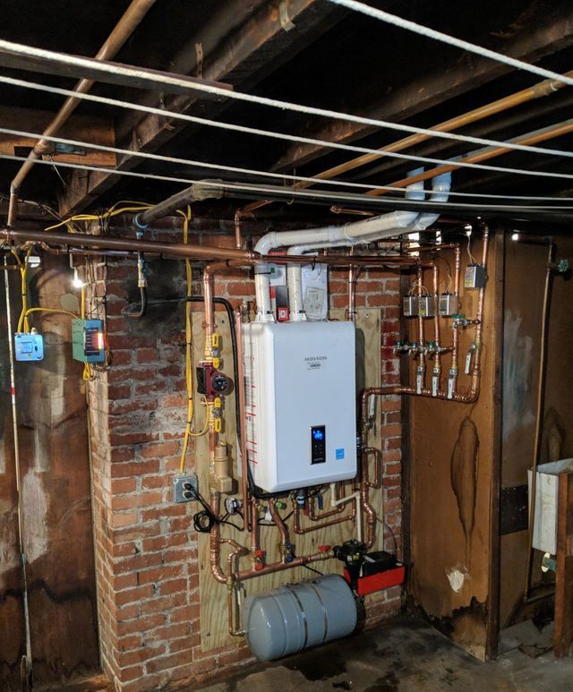 A boiler is mounted to a brick wall in a basement