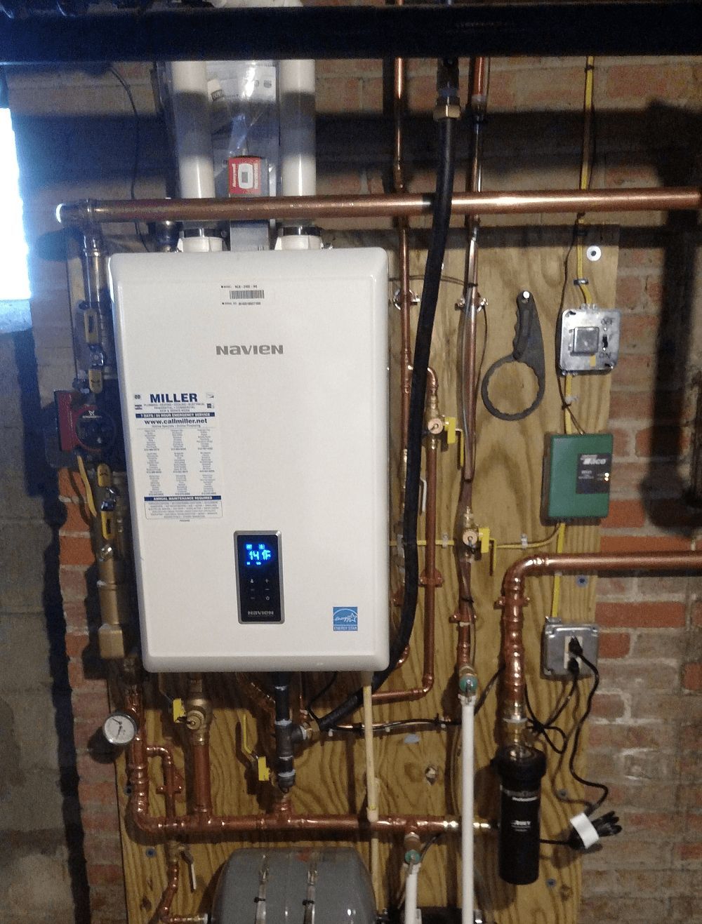 A white water heater is mounted to a brick wall