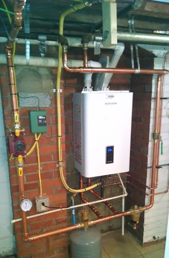 A white water heater is mounted on a brick wall next to copper pipes.