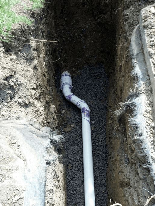 A white pipe is laying in the dirt in a trench.
