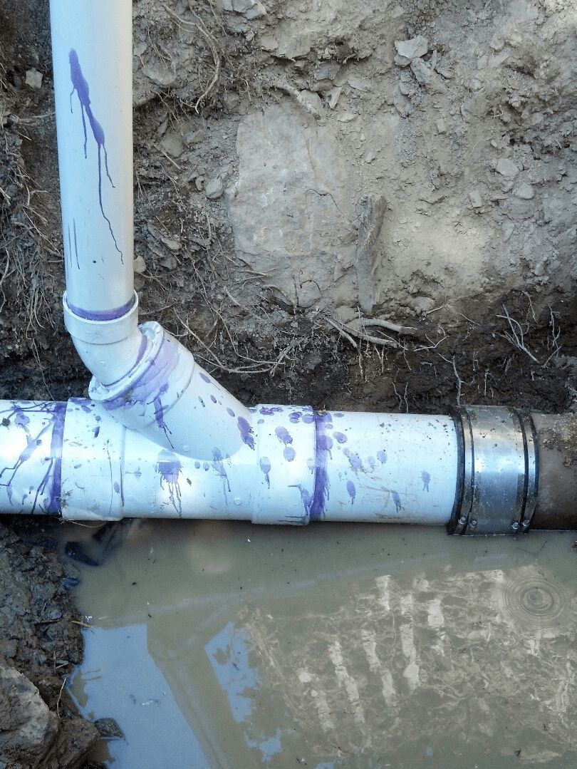 A white pipe is sitting in the dirt next to a muddy pipe.