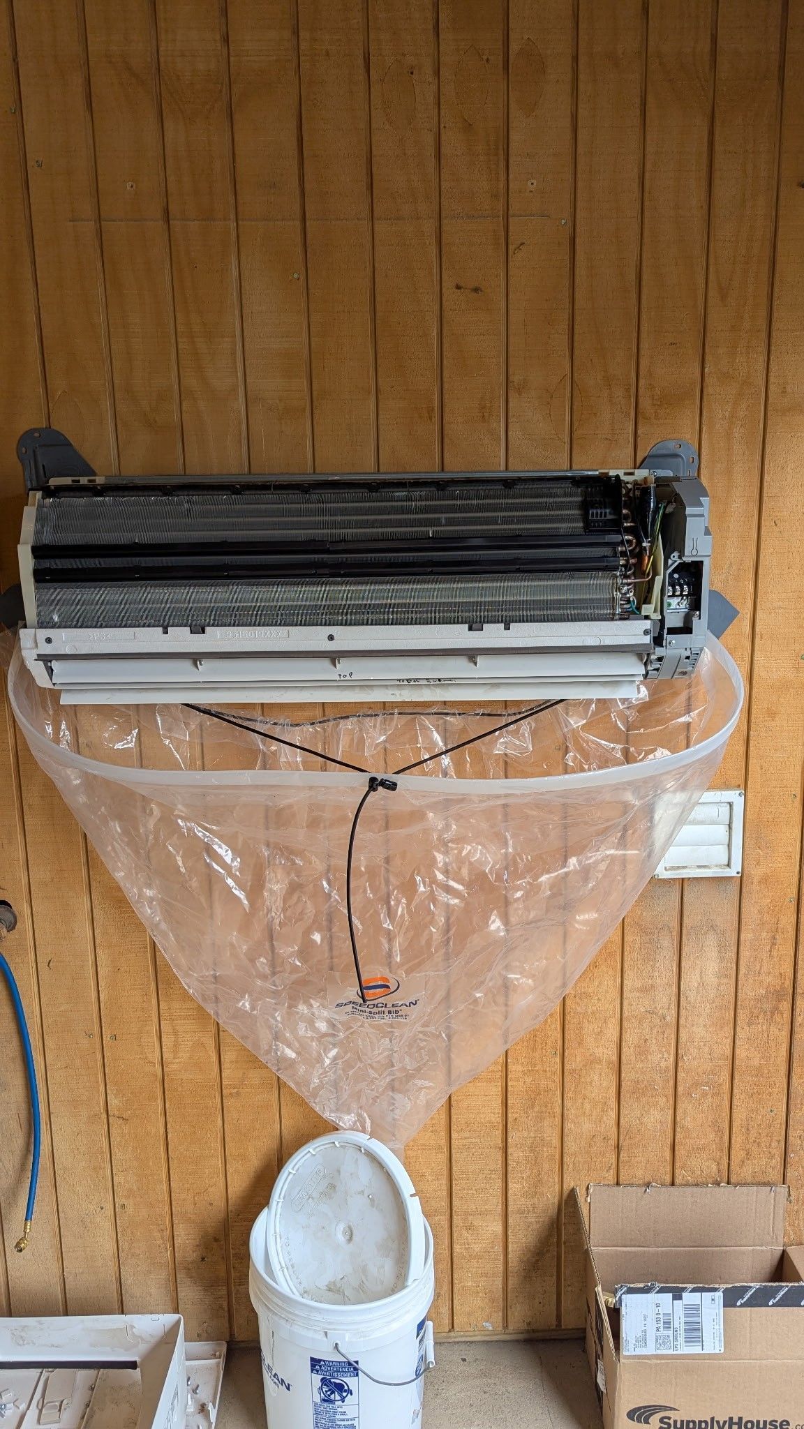 A wall mounted air conditioner is being cleaned with a plastic bag.