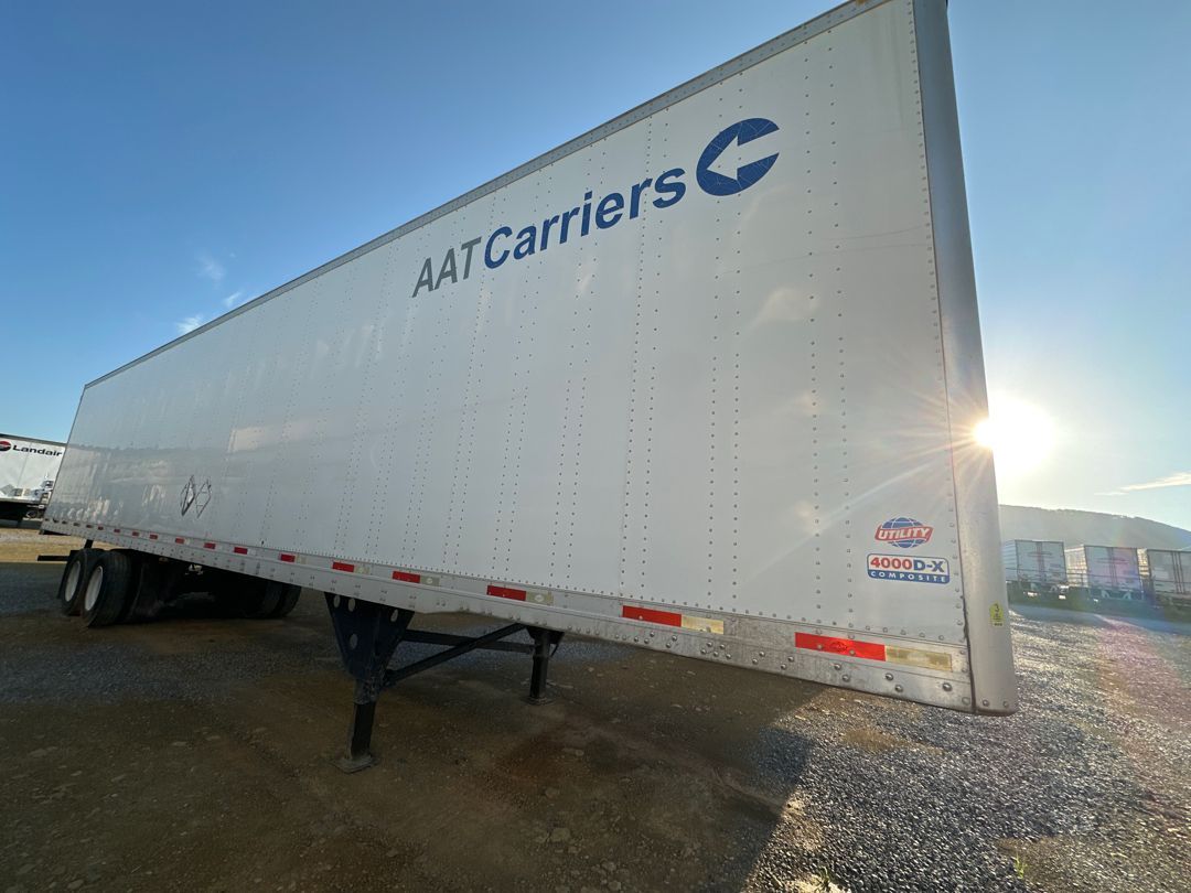 A white trailer with the word carriers on it is parked in a gravel lot.