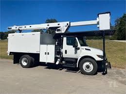 A white utility truck with a ladder on top of it is parked on the side of the road.