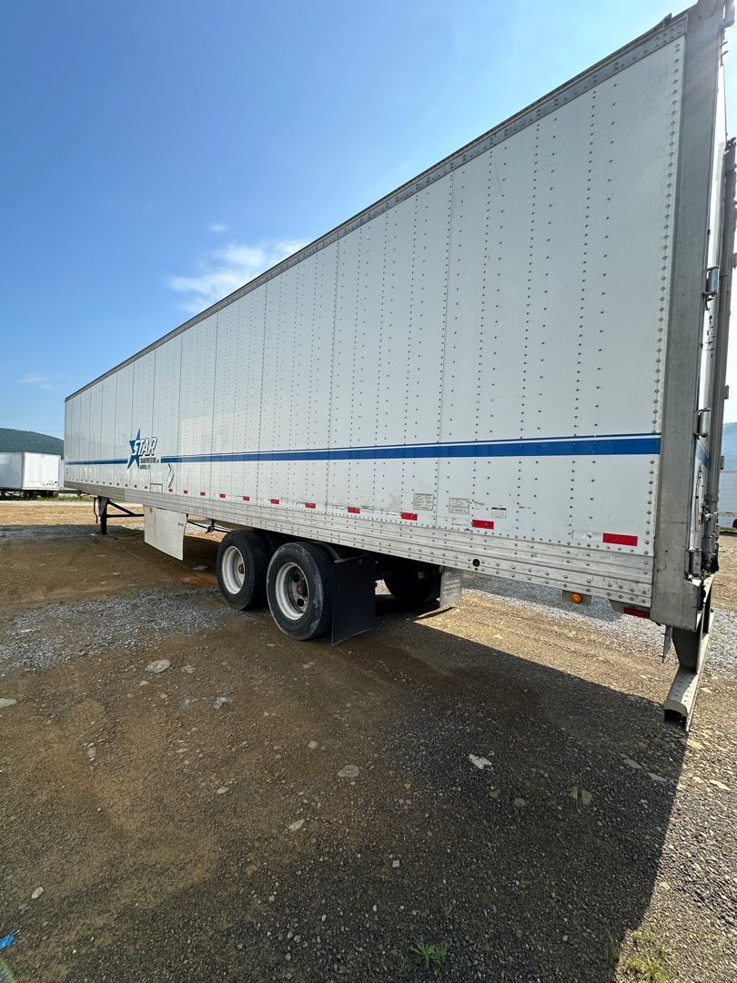 A white trailer is parked in a gravel lot.