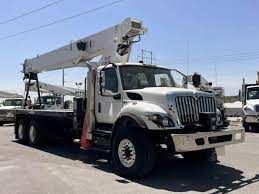 A white truck with a crane on top of it is parked on the side of the road.