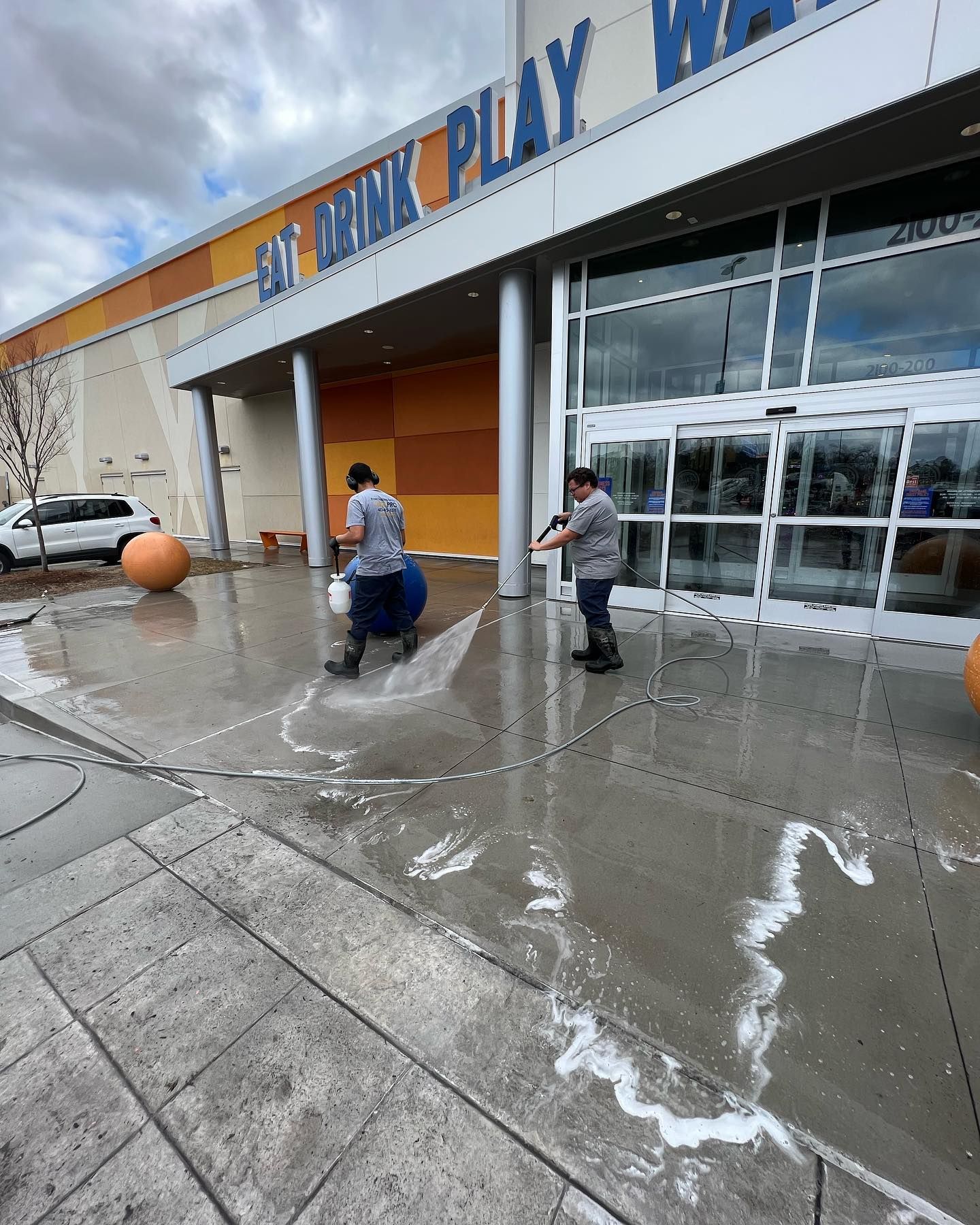 Two men are cleaning the sidewalk in front of a building.