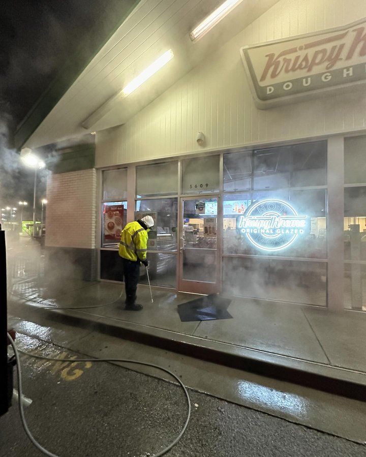 A man is cleaning the outside of a krispy kreme doughnut shop.