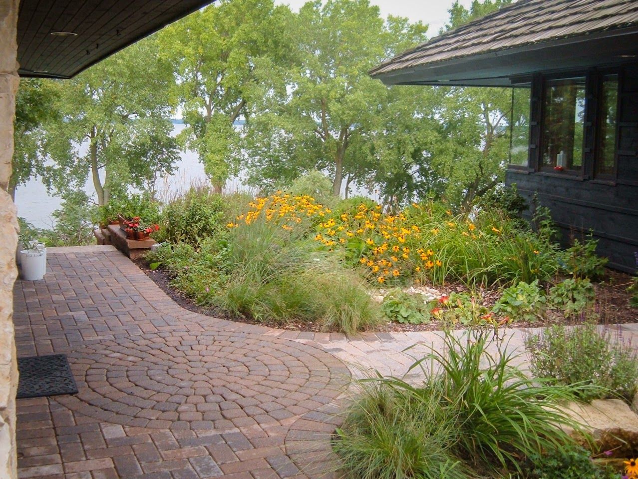 A brick walkway leading to a house with a lake in the background.