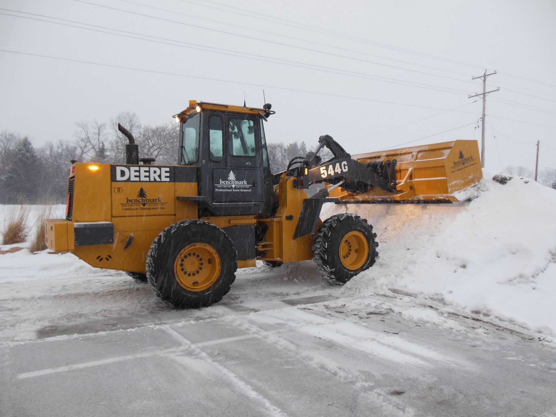 A yellow deere snow plow is clearing snow from a parking lot