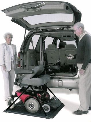 a man and a woman are standing next to a car with a scooter in the back