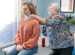 a woman is sitting on a table getting her neck examined by a therapist