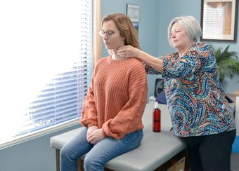 a woman is sitting on a table getting her neck examined by a therapist