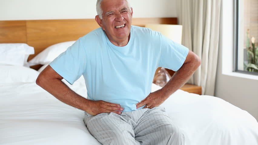 an elderly man is sitting on a bed with his hands on his hips