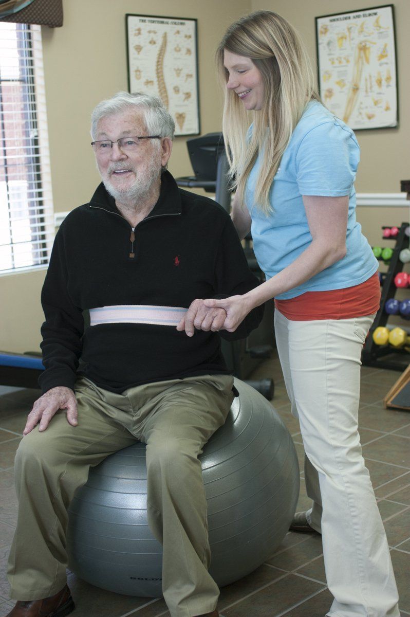 a woman helps an older man on an exercise ball